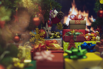 Pile of shiny luxury colorful gift boxes. Christmas and new year celebrate gifts stack beside full decorated Xmas tree with flame of fire in fireplace blur in background to give for family members