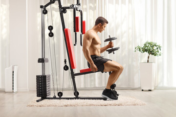 odybuilder shirtless sitting and exercising on a fitness machine indoors