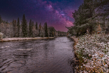Blended image of nighttime river landscape near Mörkret in Sweden with coniferous forests along the banks and small rapids in the flowing water against a background with clear starry sky © photodigitaal.nl