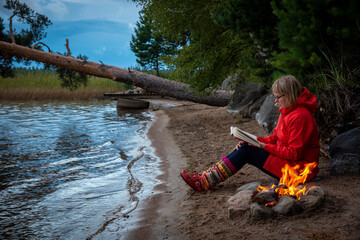 Woman sitting by the fire on the lake beach