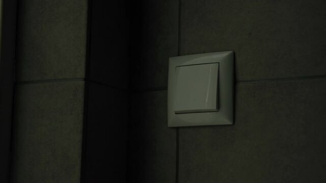 electrical energy, young women turn off bathroom light after use with switch on wall, close-up