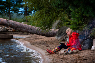 Woman sitting by the fire on the lake beach