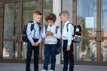 Three little schoolchildren stand at the school and look at the phone