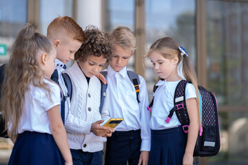 A group of little schoolchildren stands at the school and looks at the phone