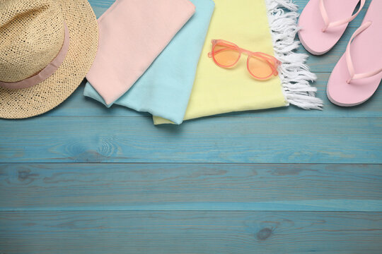 Beach towel, flip flops, straw hat and sunglasses on light blue wooden background, flat lay. Space for text