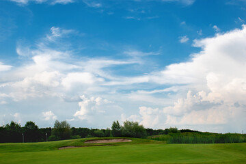 Fototapeta na wymiar Beautiful green golf course with amazing blue sky, white clouds and distant trees background
