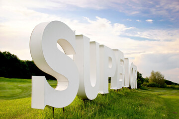 White three-dimensional 3d letters forming the word SUPERIOR on green grass outdoors on a nice...