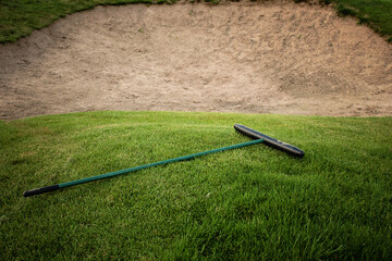 Golf course with a sand bunker, green grass and rake