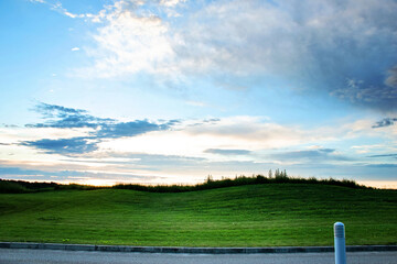 Fototapeta premium Evening landscape with blue sky, white clouds, hills covered with green grass and asphalt road
