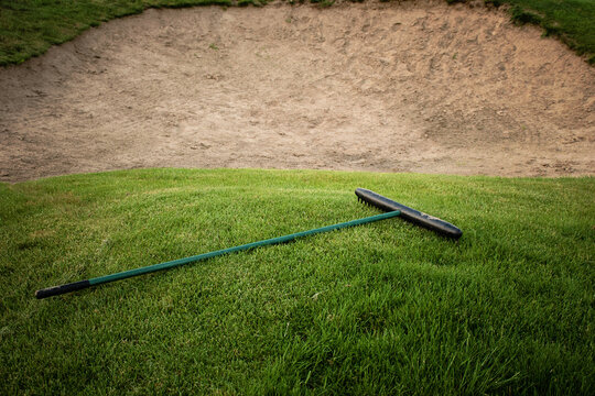 Golf course with a sand bunker, green grass and rake