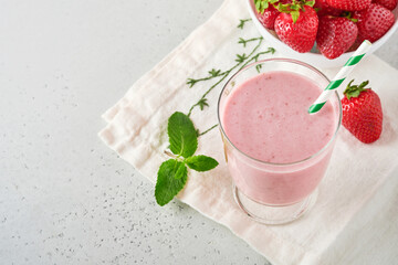Strawberry smoothie or milkshake with berries and mint in tall glass on light grey background. Summer drink shake, milkshake and refreshment organic concept. Place for text.