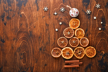 Christmas fir tree made from shaped cinnamon and dry oranges slices with red and green Christmas balls on wood background for your xmas greetings. Top view with copy space.