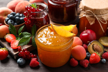 Jars with different jams and fresh fruits on wooden table, closeup