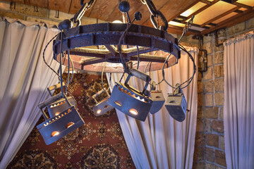 round chandelier from old irons on the background of the wall with curtains and carpet, side view