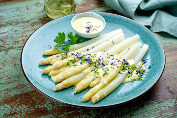 Modern style traditional steamed white asparagus garnished with sauce hollandaise and herbs served as close-up on a design plate