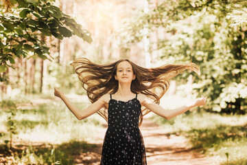 Little happy and cheerful girl with long developing hair in nature in the summer