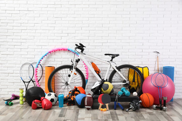 Bicycle and different sport equipment near white brick wall
