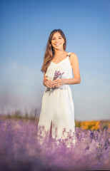 Fototapeta na wymiar Joyful and happy young beautiful woman in white dress in a lavender field.