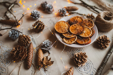 Obraz na płótnie Canvas Christmas New Year top view of handmade crafts with pine cones, dry round slices of oranges, garland, branches. New year holiday, celebration concept. Flatlay
