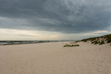 Empty beach in the evening with dramatic rain clouds over the sea, sand dunes and the beach. Landscape photo of Sandhammaren beach in Skåne, Sweden.