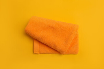 Folded orange beach towel on yellow background, top view