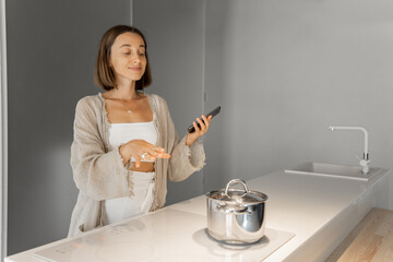 Young stylish woman cooking on induction hob at modern kitchen. Concept of smart technologies of...