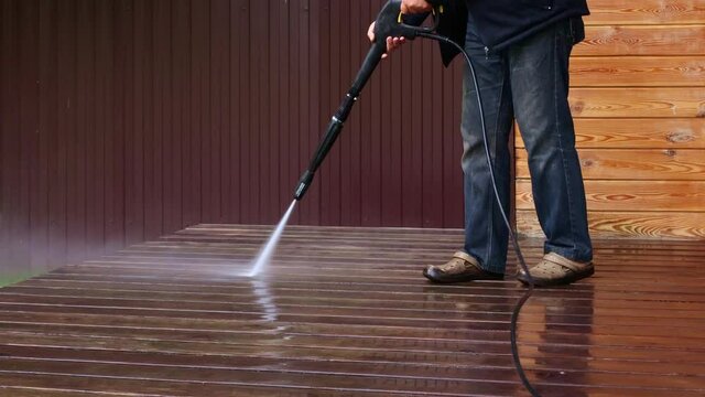 Man cleaning walls and floor with high pressure power washer. Washing terrace wood planks and cladding walls.