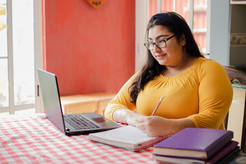 Young hispanic woman studying at home - concentrated college student studying online - woman...
