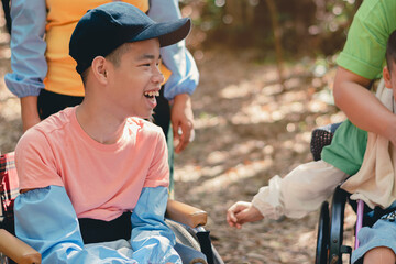 Smart handicapped teenager boy on wheelchair and friends on nature outdoors with sensory therapy in hiking, Lifestyle of disabled kids with school of special children.