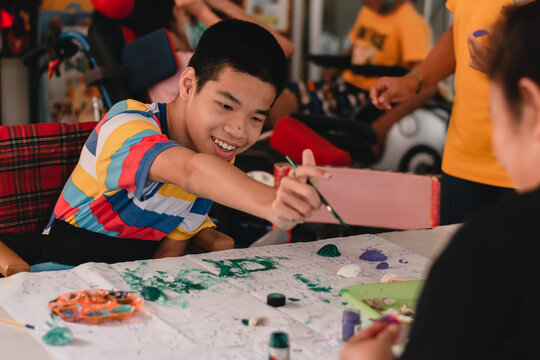 Handicapped teenager boy on wheelchair with happy face doing art work with friends, Lifestyle of smart disabled kid learning activity in special children school, Mental health classroom concept.
