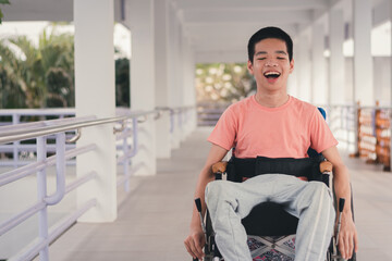 Confident handicapped teenager boy on wheelchair with happy face on walk way in hospital, Smart...