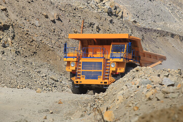Large yellow mining dump truck on the road on a sunny day. Large-sized equipment for the transportation of rock mass in an ore quarry.