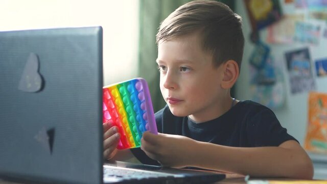 Caucasian boy in front of a laptop at home studies in the breaks between classes, plays pop it. Distance learning schoolchildren theme. A child of 6-8 years old is studying on a laptop. selective focu