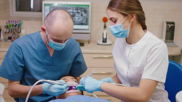 female patient have a visiting at the dental clinic dentist man and his assistant lady treat the caries of patient they wearing protective mask