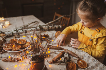 A cute sweet girl makes Christmas decorations from dried oranges, twigs and cones. Crafts for the holiday