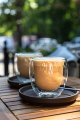 Cappuccino with latte art in glass cup on wooden table in outdoor cafe or coffeehouse. Sunny morning.