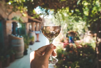 Fototapete Mittelmeereuropa Glass of wine in hand. A glass of young fresh rose wine against the backdrop of a summer cafe in a Mediterranean seaside tourist town in the summer under sunlight. Summer, travel, lifestyle