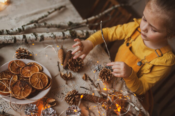 A cute sweet girl makes Christmas decorations from dried oranges, twigs and cones. Crafts for the holiday