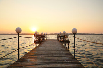 Picturesque view of empty wooden pier with lanterns at sunset