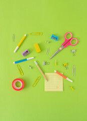 September , back to school, office concept. Various school  office supplies.  arrangement  of pencils , tapes, erasers, pins, rulers, markers, paper clips, yellow posit note . Bright green background.