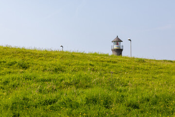 Lighthouse top behind a grass-covered dike on the North Sea 