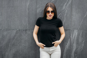 Stylish brunette girl wearing black t-shirt and glasses posing against street , urban clothing...