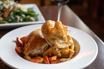 Roasted chicken, roasted vegetables, salad and wine on a table at a restaurant