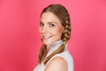 Close up portrait of young attractive smiling girl with pigtails standing isolated over pink background