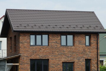 brown brick facade of a large private house with windows and a door under a tiled roof against a gray sky