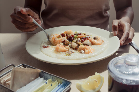Person eating a bowl of shrimp and grits inside of a restaurant