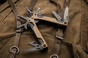 Modern multitool with many tools. A portable multitasking tool on a vintage canvas backpack. - obrazy, fototapety, plakaty