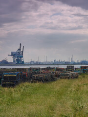 Fototapeta na wymiar Lobster pots stacked ready for use on a grass embankment by Paddy’s Hole, with the massive container cranes of Teesport looming in the background.