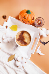 Halloween celebration coffee on the tray with smiling pumpkin, candle, coconut flowers and bats on the orange background. Halloween service. Trick or Treat! Eat, drink, and be scary. Happy Howloween. 