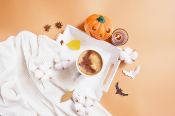 Halloween celebration coffee on the tray with smiling pumpkin, candle, coconut flowers and bats on the orange background. Halloween service. Trick or Treat! Eat, drink, and be scary. Happy Howloween. 